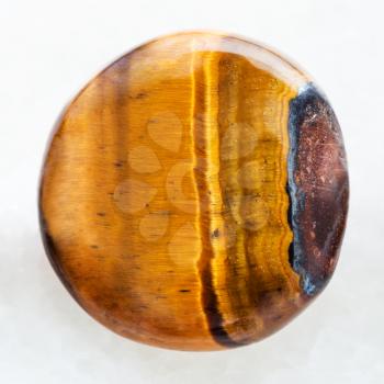 macro shooting of natural mineral rock specimen - bead from Tiger's eye gemstone on white marble background