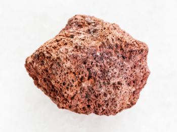 macro shooting of natural mineral rock specimen - tumbled red pumice stone on white marble background from Sicily