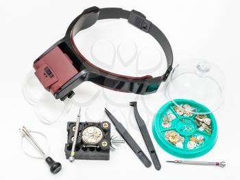 watchmaker workshop - above view of various tools with head-mounted magnifier and spare parts for repairing mechanical watch on white background