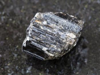 macro shooting of natural mineral rock specimen - rough crystal of Schorl (black tourmaline) gemstone on dark granite background from Madagascar