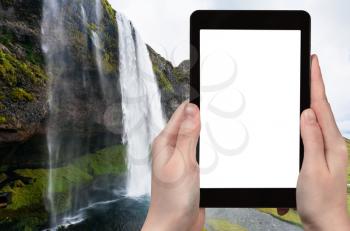 travel concept - tourist photographs Seljalandsfoss waterfall of Seljalands River in Katla Geopark in Iceland in autumn on tablet with cut out screen for advertising logo
