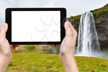 travel concept - tourist photographs Seljalandsfoss waterfall of Seljalands River in Katla Geopark on Icelandic Atlantic South Coast in autumn on tablet with cut out screen for advertising logo