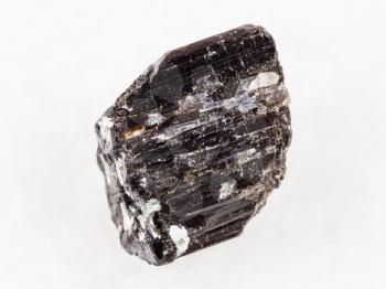 macro shooting of natural mineral rock specimen - rough crystal of Schorl (black tourmaline) gemstone on white marble background from Madagascar