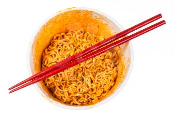 red chopsticks over cup with prepared spicy instant noodles isolated on white background