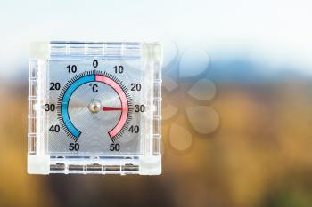 view of outdoor thermometer on home window and blurred skyline with forest in hot autumn day
