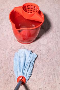 point of view of mop cleans linoleum floor near red bucket with water at home