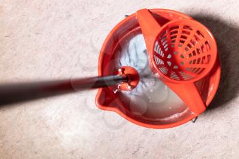 top view of mop rinsing in red bucket with water at home