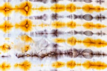 textile background - abstract yellow and brown ornament in tie-dye batik technique on white silk fabric of handcrafted scarf