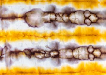 textile background - abstract spotted yellow and brown pattern in tie-dye batik technique on white silk fabric of handcrafted scarf