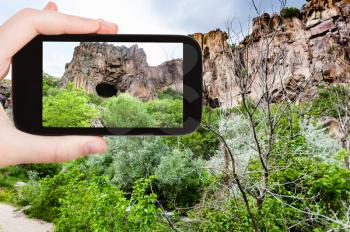 travel concept - tourist photographs of mountain cave in Ihlara Valley of Aksaray Province in Cappadocia on smartphone in Turkey in spring