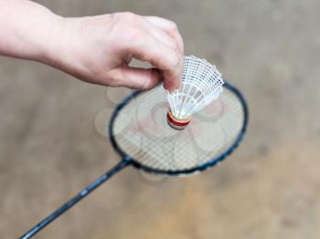hand holds white shuttlecock over badminton racquet on outdoor earth ground