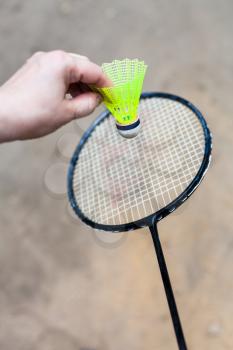 hand holds yellow shuttlecock over badminton racquet on outdoor earth ground