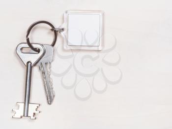two door keys on keyring with blank white keychain on pale brown table