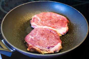 frying two piece of meat in pan on ceramic electric range at home kitchen
