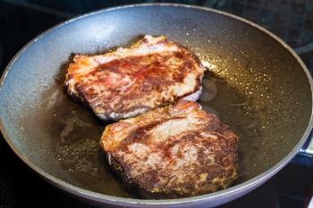 two roasted piece of meat in frying pan on ceramic electric range at home kitchen