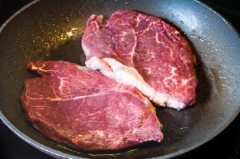 roasting two beefsteaks in frying pan on ceramic electric range at home kitchen