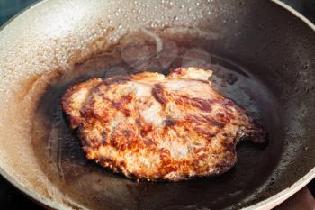 roasting beef steak in frying pan on ceramic electric range at home kitchen