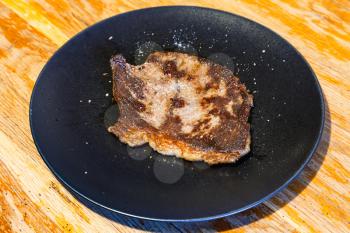 piece of roasted meat on black plate on wooden table at home kitchen