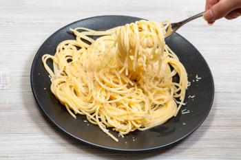 winding spaghetti al burro e parmigiano (pasta with butter and cheese) on fork over black plate on gray wooden table