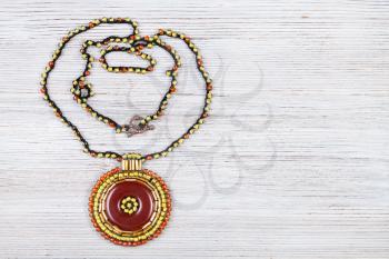 needlecraft background - handcrafted necklace with round brown leather pendant embroidered by glass beads and bugles on gray wooden board with copyspace