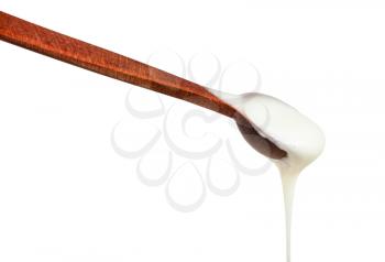 side view of natural organic white honey flows from little wooden spoon close up isolated on white background
