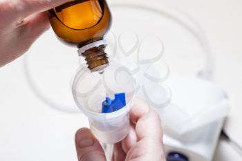 woman dripping medicine from glass bottle into nebulizer close up