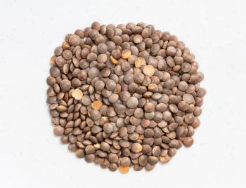 top view of pile of raw brown unhulled red lentils close up on gray ceramic plate