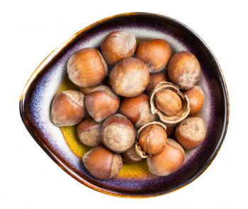 top view of shelled and whole hazelnuts in ceramic bowl isolated on white background