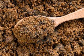 top view of wood spoon with dark muscovado cane sugar close up on pile of sugar