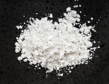 top view of pile of vanilla sugar (sugar powder with ground natural vanilla) close up on black ceramic plate