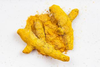 top view of pile of Turmeric (Curcuma) powder and roots close up on gray ceramic plate