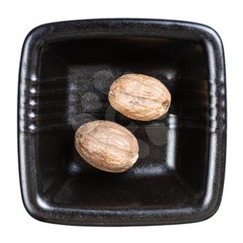 top view of two whole nutmegs in black bowl isolated on white background