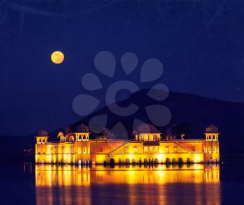 Vintage retro hipster style travel image of Rajasthan landmark - Jal Mahal (Water Palace) on Man Sagar Lake at night in twilight with grunge texture overlaid.  Jaipur, Rajasthan, India