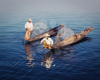 Myanmar travel attraction - Traditional Burmese fishermen with fishing net at Inle lake in Myanmar famous for their distinctive one legged rowing style. Vintage filtered retro effect hipster style ima