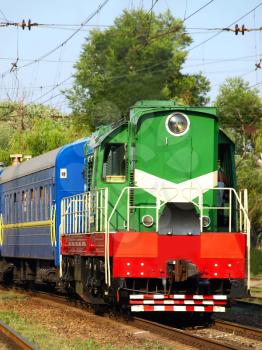 Green locomotive and blue passenger cars on the rails taken closeup.