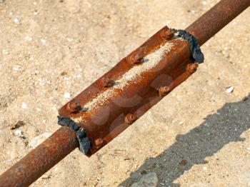 Damaged rusty water pipe on a sand background.