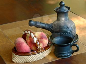 Arabian coffee pot and ceramic vase with peaches on a table.