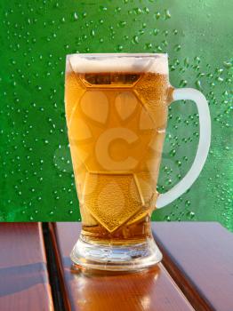 Beer glass on wooden table on green drips abstract background.
