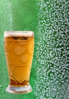 Froth beer glass on ice crystals and drips green background.