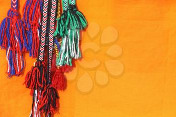 Colorful tassels of a hippie belts taken closeup on orange background.
