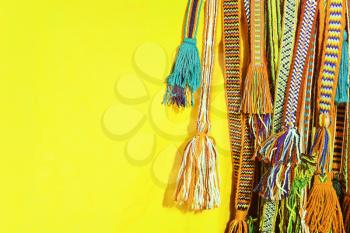 Multicolored tassels of a hippie belts taken closeup on yellow background.