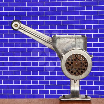Old meat grinder on blue brick wall background taken closeup.