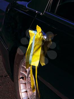 Yellow wedding ribbon on black car door taken closeup.