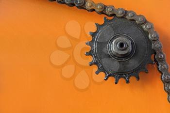 Metal cogwheel with chain taken closeup on orange background.