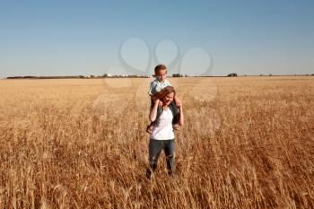 Young boy riding on shoulders of mother in wheat crop