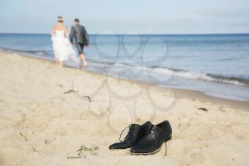 Just married couple walking on the seashore with focus on the man's shoes