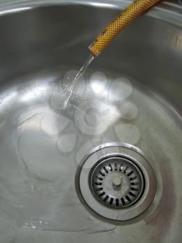 Water flowing from the plastic hose in a sink metal close-up