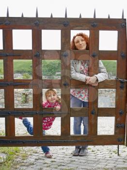 Woman and a small girl are posing behind a wooden gate with wrought iron elements