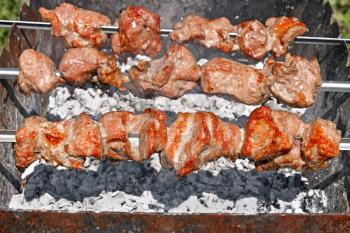 Shashlyk (shish kebab) prepared on the still skewers over hot charcoal with ash outdoors, European and Asian traditional dish