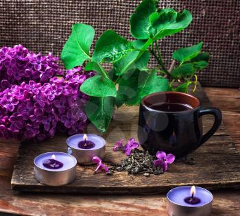 Cup of tea,three candles,branch of blossoming lilac on wooden surface